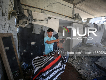 A barber is cutting the hair of a man in the ruins of his destroyed salon, which was destroyed by Israeli strikes, in al-Bureij refugee camp...