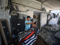 A barber is cutting the hair of a man in the ruins of his destroyed salon, which was destroyed by Israeli strikes, in al-Bureij refugee camp...