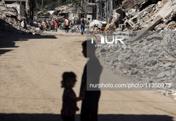 Palestinians are making their way past destroyed buildings in al-Bureij refugee camp in the central Gaza Strip, on June 22, 2024, amid the o...