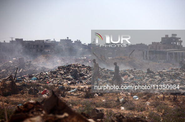 Palestinian men are searching for recyclables at a garbage dump in al-Bureij refugee camp in the central Gaza Strip, on June 22, 2024, amid...