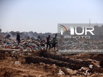 Palestinian men are searching for recyclables at a garbage dump in al-Bureij refugee camp in the central Gaza Strip, on June 22, 2024, amid...