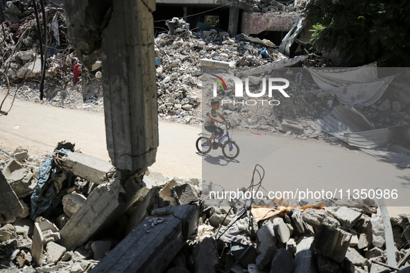 A Palestinian boy is riding his bicycle past destroyed buildings in al-Bureij refugee camp in the central Gaza Strip, on June 22, 2024, amid...