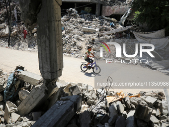 A Palestinian boy is riding his bicycle past destroyed buildings in al-Bureij refugee camp in the central Gaza Strip, on June 22, 2024, amid...