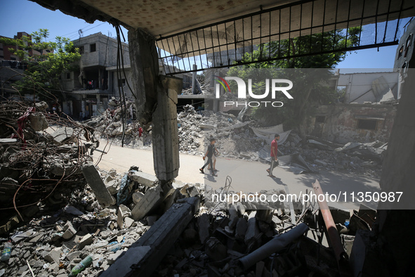 Palestinians are making their way past destroyed buildings in al-Bureij refugee camp in the central Gaza Strip, on June 22, 2024, amid the o...