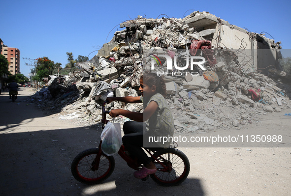 A Palestinian girl is riding her bicycle past destroyed buildings in al-Bureij refugee camp in the central Gaza Strip, on June 22, 2024, ami...