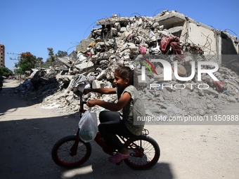 A Palestinian girl is riding her bicycle past destroyed buildings in al-Bureij refugee camp in the central Gaza Strip, on June 22, 2024, ami...