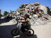 A Palestinian girl is riding her bicycle past destroyed buildings in al-Bureij refugee camp in the central Gaza Strip, on June 22, 2024, ami...