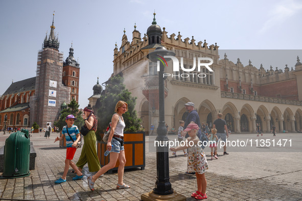 People walk by a water mist sprinkler at the Main Square in Krakow, Poland on June 21, 2024. 