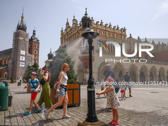 People walk by a water mist sprinkler at the Main Square in Krakow, Poland on June 21, 2024. (