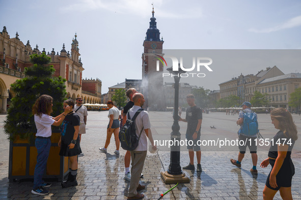 People walk by a water mist sprinkler at the Main Square in Krakow, Poland on June 21, 2024. 