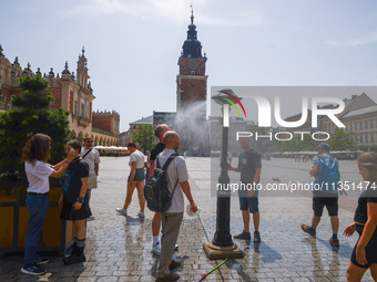 People walk by a water mist sprinkler at the Main Square in Krakow, Poland on June 21, 2024. (