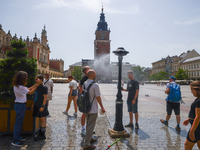 People walk by a water mist sprinkler at the Main Square in Krakow, Poland on June 21, 2024. (