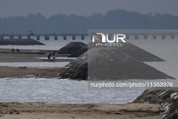 Workers are scooping up oil-stained sand at East Coast Park beach in Singapore, on June 23, 2024. Singapore authorities are continuing clean...