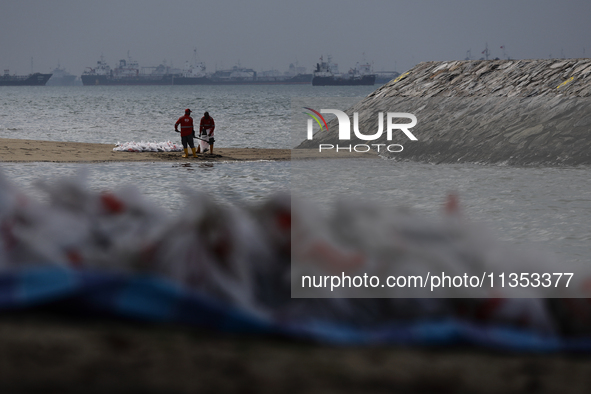 Workers are scooping up oil-stained sand at East Coast Park beach in Singapore, on June 23, 2024. Singapore authorities are continuing clean...