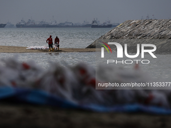 Workers are scooping up oil-stained sand at East Coast Park beach in Singapore, on June 23, 2024. Singapore authorities are continuing clean...