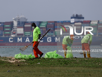 Workers are scooping up oil-stained sand at East Coast Park beach in Singapore, on June 23, 2024. Singapore authorities are continuing clean...