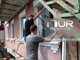 Men are sealing a knocked-out window with a film after a Russian missile attack in Vasylkiv, Ukraine, on June 23, 2024. On Sunday morning, J...