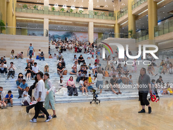 People are sitting on the steps of the hall of Shandong Museum to cool off in Jinan, China, on June 23, 2024. (