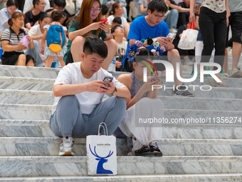 People are sitting on the steps of the hall of Shandong Museum to cool off in Jinan, China, on June 23, 2024. (