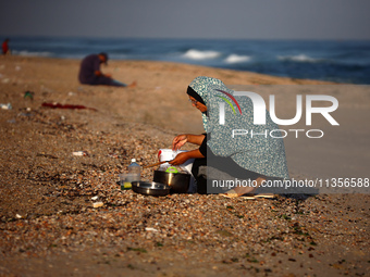 A Palestinian woman is washing kitchenware on the beach in Deir el-Balah, central Gaza Strip, on June 24, 2024, amid the ongoing conflict be...