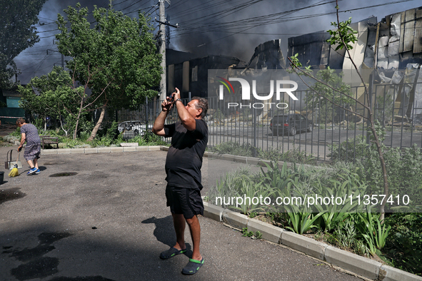 A man is taking a picture as smoke is rising from a warehouse destroyed as a result of a Russian missile strike in Odesa, Ukraine, on June 2...