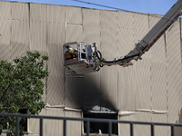 Firefighters in an aerial ladder platform are putting out a fire at a warehouse caused by a Russian missile attack on civilian infrastructur...