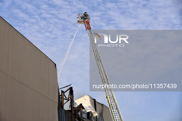 A firefighter in an aerial ladder platform is putting out a fire at a warehouse caused by a Russian missile attack on civilian infrastructur...