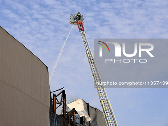 A firefighter in an aerial ladder platform is putting out a fire at a warehouse caused by a Russian missile attack on civilian infrastructur...