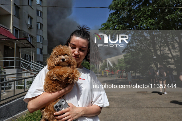 A woman is holding a dog as smoke is rising from a warehouse destroyed as a result of a Russian missile strike in Odesa, Ukraine, on June 24...