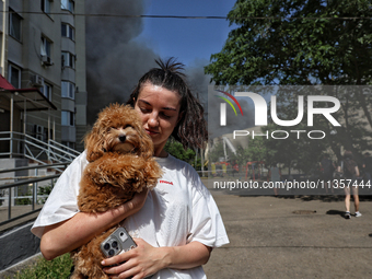 A woman is holding a dog as smoke is rising from a warehouse destroyed as a result of a Russian missile strike in Odesa, Ukraine, on June 24...