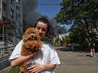 A woman is holding a dog as smoke is rising from a warehouse destroyed as a result of a Russian missile strike in Odesa, Ukraine, on June 24...