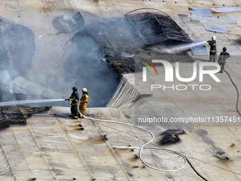 Firefighters are seen on the roof of a warehouse as they are putting out a fire caused by a Russian missile strike in Odesa, Ukraine, on Jun...