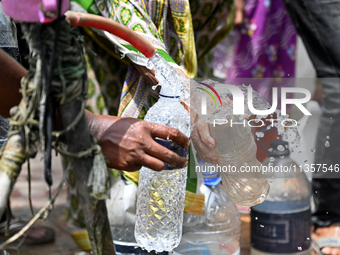 People are gathering around a roadside water pipeline to collect drinking water during a high-temperature weather day in Dhaka, Bangladesh,...