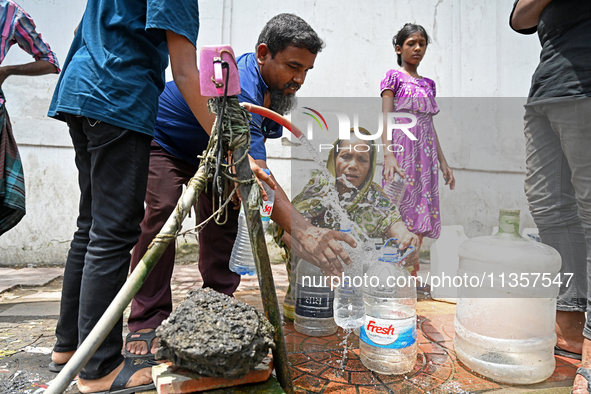 People are gathering around a roadside water pipeline to collect drinking water during a high-temperature weather day in Dhaka, Bangladesh,...