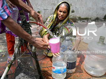 People are gathering around a roadside water pipeline to collect drinking water during a high-temperature weather day in Dhaka, Bangladesh,...