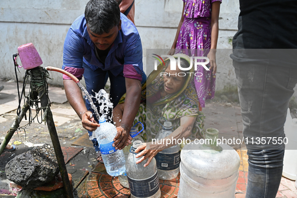 People are gathering around a roadside water pipeline to collect drinking water during a high-temperature weather day in Dhaka, Bangladesh,...