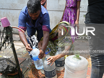 People are gathering around a roadside water pipeline to collect drinking water during a high-temperature weather day in Dhaka, Bangladesh,...