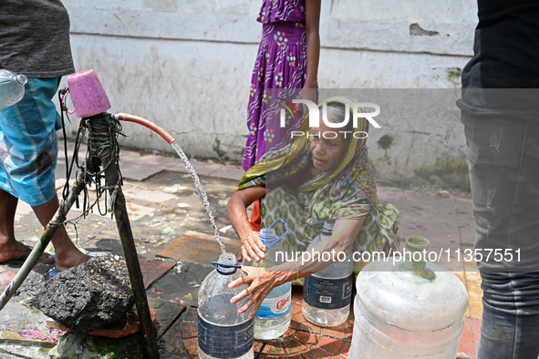 People are gathering around a roadside water pipeline to collect drinking water during a high-temperature weather day in Dhaka, Bangladesh,...