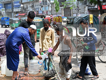 People are gathering around a roadside water pipeline to collect drinking water during a high-temperature weather day in Dhaka, Bangladesh,...