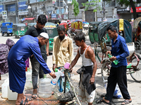 People are gathering around a roadside water pipeline to collect drinking water during a high-temperature weather day in Dhaka, Bangladesh,...