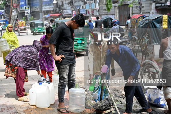 People are gathering around a roadside water pipeline to collect drinking water during a high-temperature weather day in Dhaka, Bangladesh,...