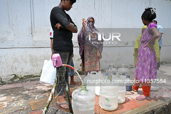 People are gathering around a roadside water pipeline to collect drinking water during a high-temperature weather day in Dhaka, Bangladesh,...