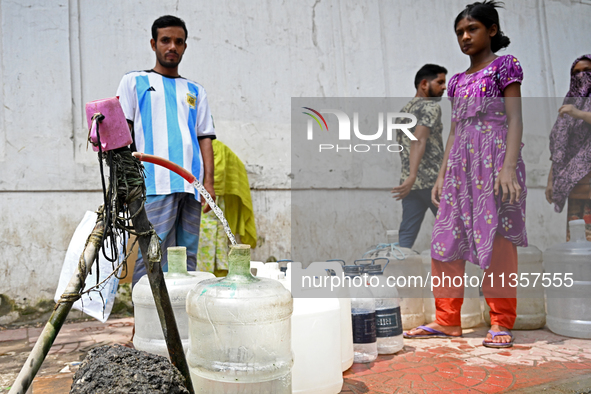 People are gathering around a roadside water pipeline to collect drinking water during a high-temperature weather day in Dhaka, Bangladesh,...