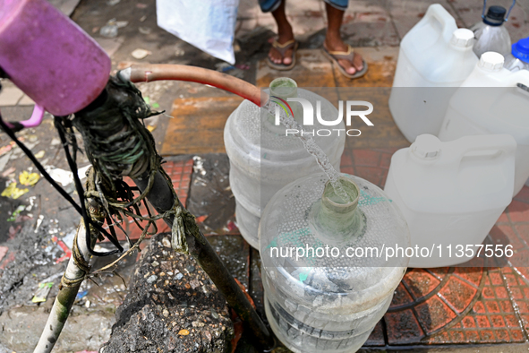 People are gathering around a roadside water pipeline to collect drinking water during a high-temperature weather day in Dhaka, Bangladesh,...