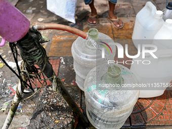 People are gathering around a roadside water pipeline to collect drinking water during a high-temperature weather day in Dhaka, Bangladesh,...