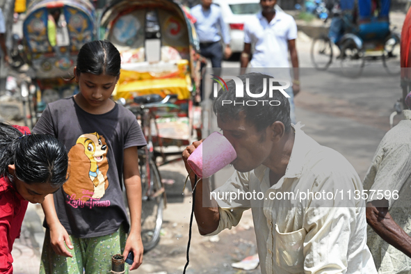 A rickshaw driver is drinking water from a roadside water pipeline during high temperature weather in Dhaka, Bangladesh, on June 24, 2024 