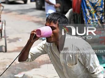 A rickshaw driver is drinking water from a roadside water pipeline during high temperature weather in Dhaka, Bangladesh, on June 24, 2024 (