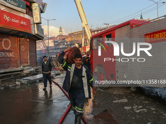 A firefighter is carrying a water hose after a fire engulfed a congested neighborhood in Old City Srinagar, Indian Administered Kashmir, on...