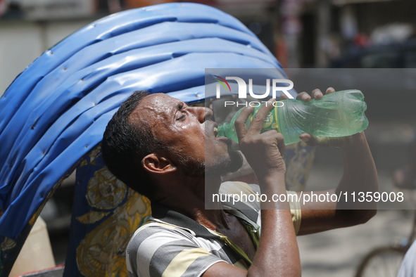 A thirsty rickshaw puller is drinking water to get relief on a hot summer day in Dhaka, Bangladesh, on June 24, 2024. 