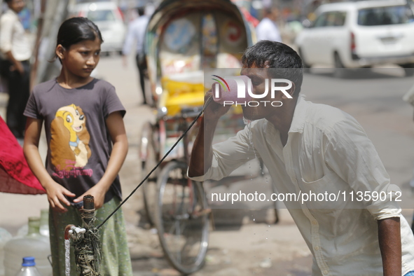 A thirsty rickshaw puller is drinking water from a roadside tap to get relief on a hot summer day in Dhaka, Bangladesh, on June 24, 2024. 